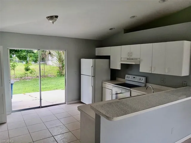 Kitchen featuring white appliances, light tile patterned floors, vaulted ceiling, white cabinets, and light countertops