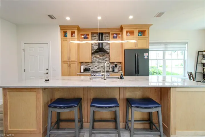 Kitchen featuring black fridge, wall chimney range hood, a spacious island, dark hardwood / wood-style floors, and tasteful backsplash