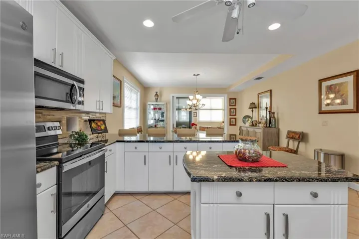 Kitchen with stainless steel appliances, light tile patterned floors, kitchen peninsula, white cabinets, and ceiling fan with notable chandelier