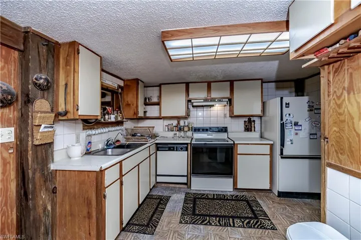 Kitchen with white appliances, light countertops, under cabinet range hood, a textured ceiling, and open shelves