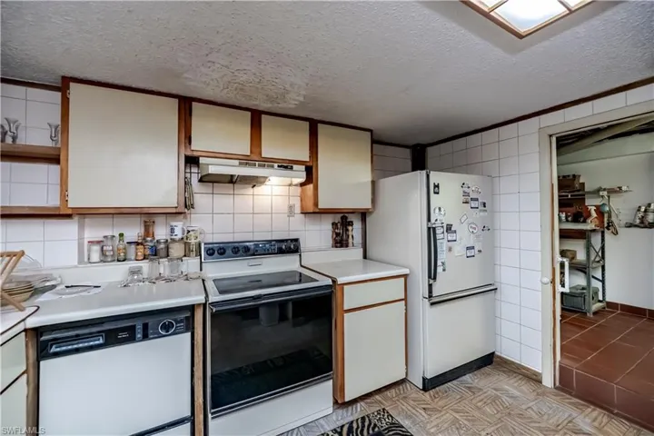 Kitchen featuring white appliances, under cabinet range hood, light countertops, a textured ceiling, and tasteful backsplash