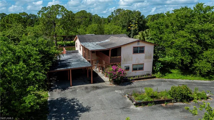 View of front of home with stairway, asphalt driveway, a view of trees, roof with shingles, and a carport