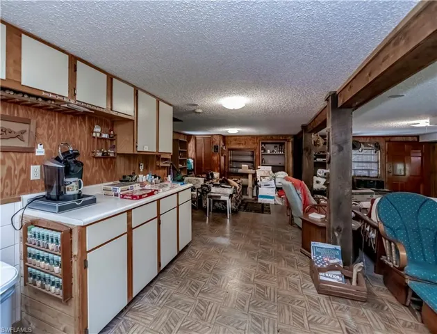 Kitchen featuring a textured ceiling, wood walls, light countertops, white cabinets, and light flooring