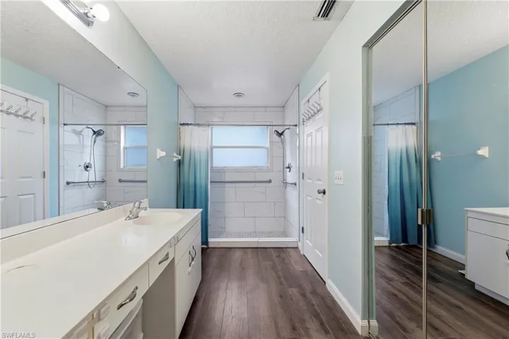 Bathroom featuring a double vanity with a white countertop, wood-finish flooring, and a tiled shower with a window