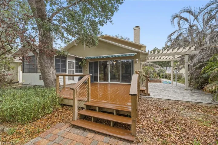 Expansive rear exterior featuring a wooden deck with cable railings, a pergola over a paver patio, and sliding glass doors