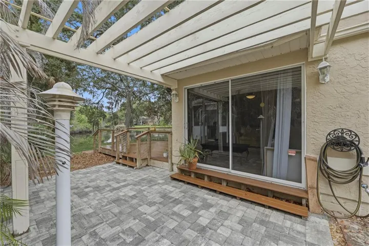 Outdoor living area featuring a pergola-covered paver patio, sliding glass door entry, and a raised wood deck with water frontage