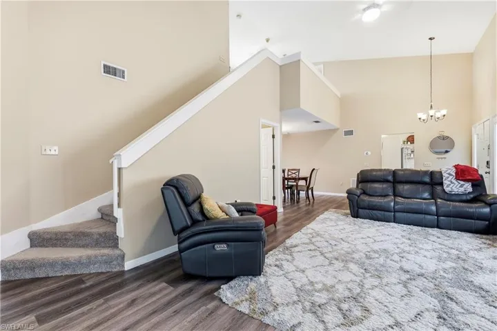 Vaulted ceilings define this spacious living area, featuring wood-finish flooring and a carpeted staircase