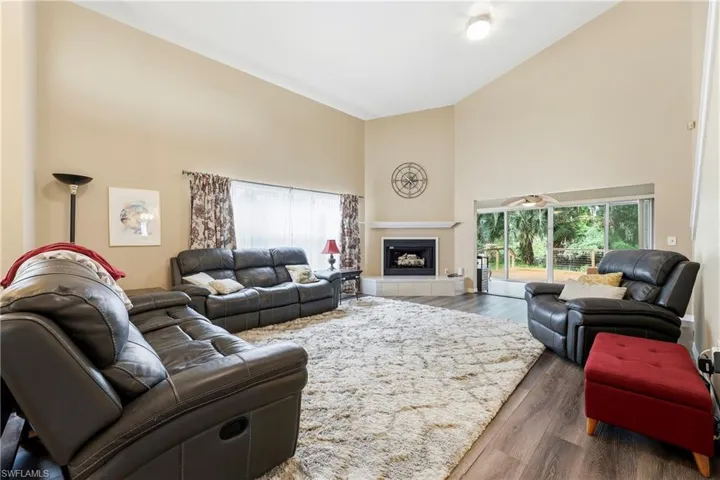 Spacious living area featuring vaulted ceilings, wood-finish flooring, and a corner fireplace with a tiled hearth