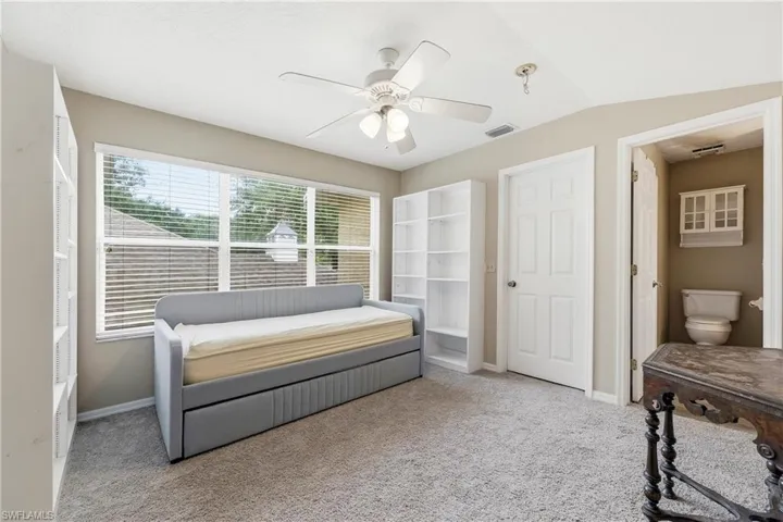 Carpeted room featuring multiple windows with horizontal blinds, a white ceiling fan, and an interior door opening to a water closet with a built-in cabinet
