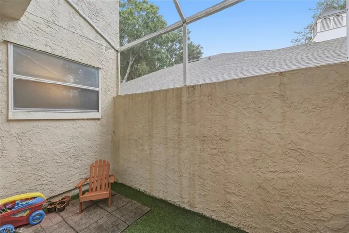 Private enclosed patio space featuring stucco exterior, screened enclosure, and a combination of artificial turf and paving stones