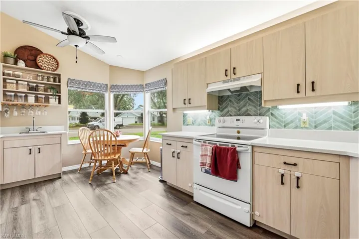 Kitchen featuring wood-finish flooring, light wood cabinetry with dark hardware, a herringbone pattern tile backsplash, and white countertops