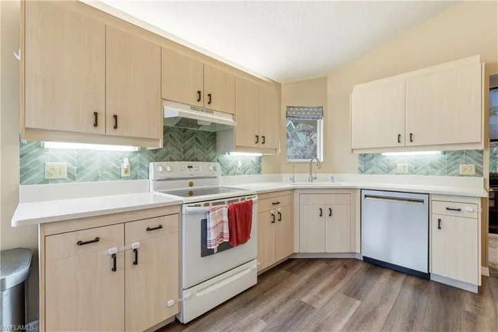 Kitchen featuring light wood-finish cabinetry with black hardware, white countertops, a chevron-patterned tile backsplash, and under-cabinet lighting