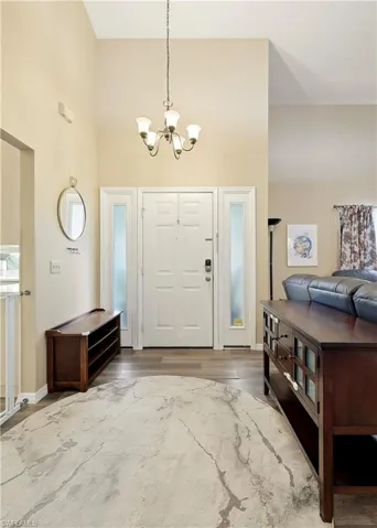 Two-story foyer with a decorative chandelier, dual sidelight windows, wood-finish flooring, and neutral wall tones
