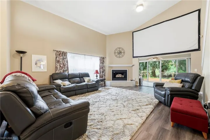 Living area featuring vaulted ceilings, wood-finish flooring, a fireplace with a mantel, a large projection screen, and sliding glass doors to the exterior