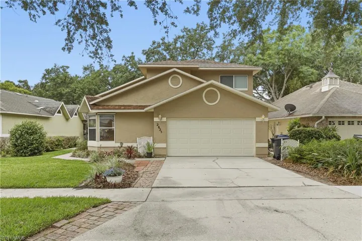 Two-story stucco home featuring a two-car garage, concrete driveway, and front lawn with mature landscaping