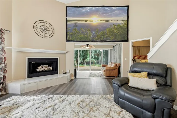 Vaulted ceiling living area featuring a fireplace with a tiled hearth, wood-finish flooring, and direct access to an enclosed patio through sliding glass doors