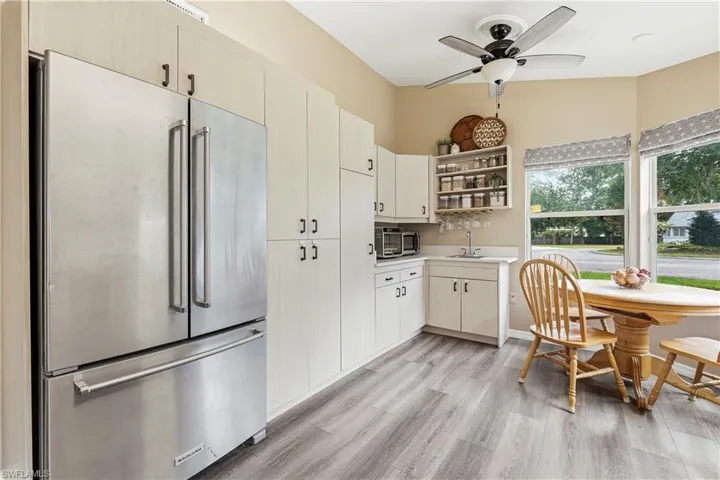 Kitchen featuring stainless steel refrigerator, light wood-finish flooring, white cabinetry, ceiling fan, and bay windows