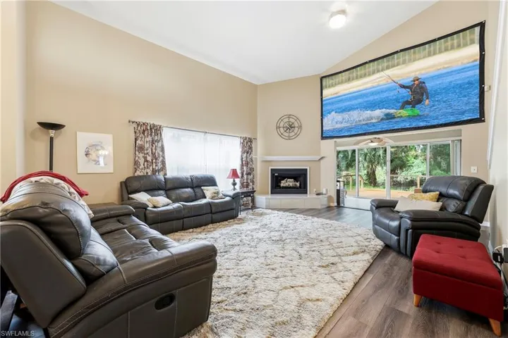 Living area featuring vaulted ceilings, a built-in fireplace with a hearth, wood-finish flooring, and a large sliding glass door