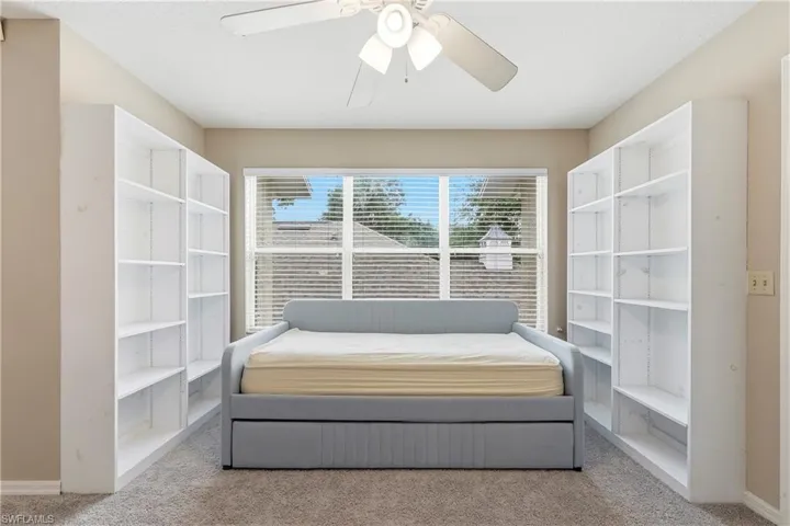 Room featuring a ceiling fan with light fixture, central window with blinds, and two built-in shelving units