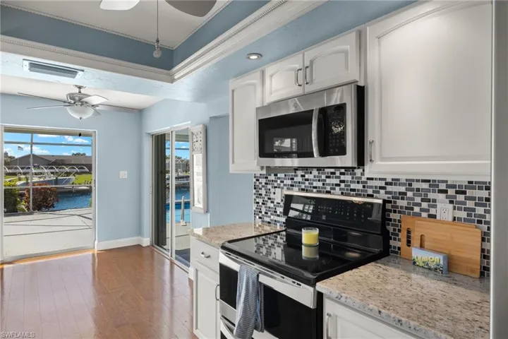 Kitchen featuring dark hardwood / wood-style floors, stainless steel appliances, white cabinetry, a water view, and tasteful backsplash