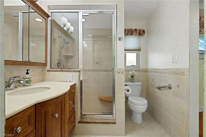 Bathroom with walk in shower, tile walls, toilet, vanity, and tile patterned flooring
