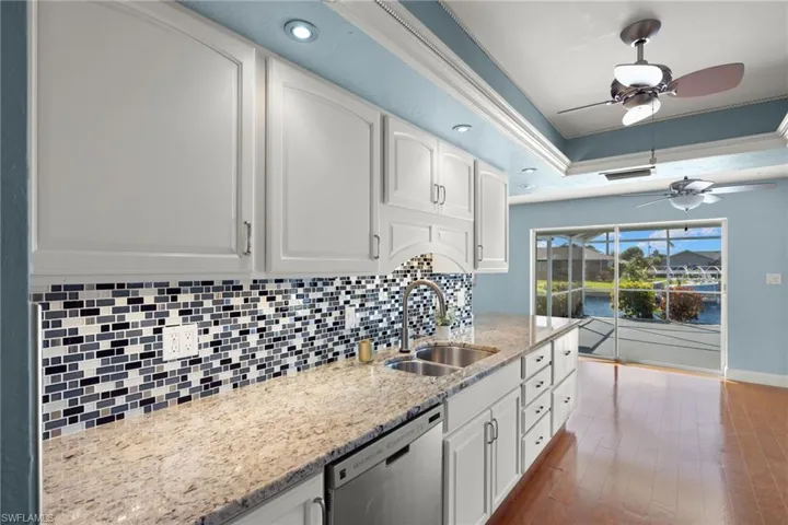 Kitchen with sink, hardwood / wood-style floors, light stone countertops, stainless steel dishwasher, and white cabinets