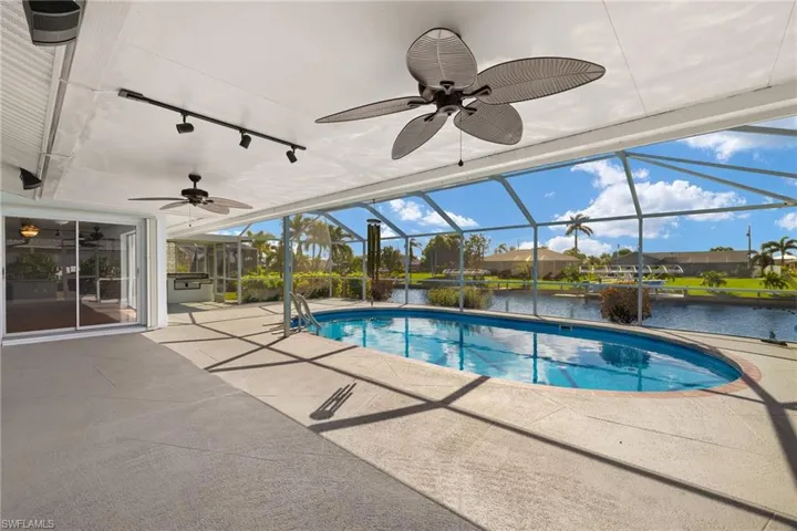 View of pool featuring a patio, ceiling fan, a water view, and glass enclosure
