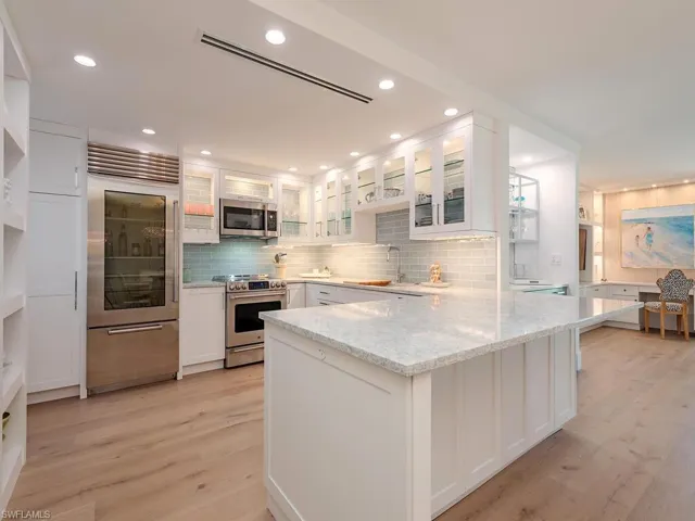 Kitchen featuring white cabinetry, appliances with stainless steel finishes, glass insert cabinets, a peninsula, and light stone counters