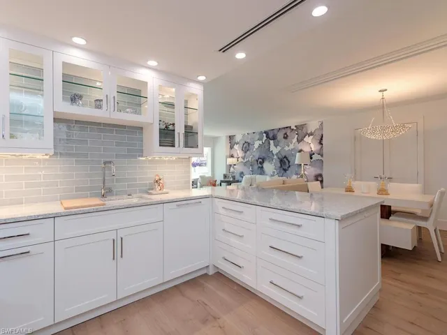 Kitchen with glass insert cabinets, white cabinets, light stone countertops, light wood finished floors, and recessed lighting