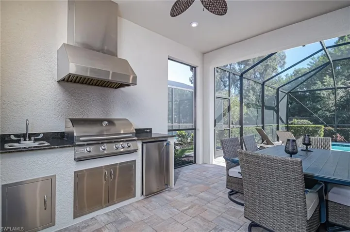 Outdoor Kitchen with grill, sink, and refridgerator, with seating to entertain- lanai has two doors to access side yards and large screened-in area