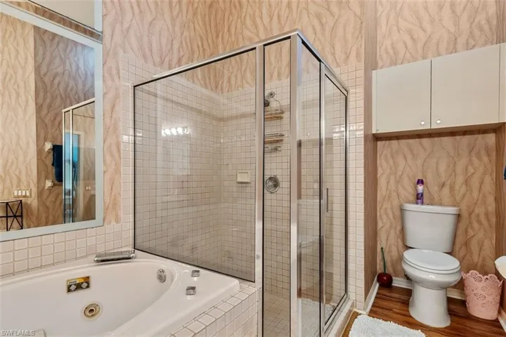 Full bath with a whirlpool tub, a shower stall, wallpapered walls, tile walls, and wood finished floors