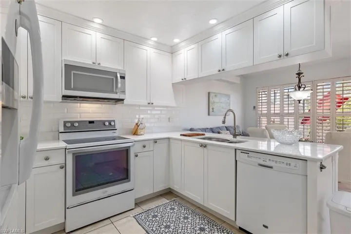 Kitchen with white appliances, a peninsula, backsplash, light countertops, and white cabinetry