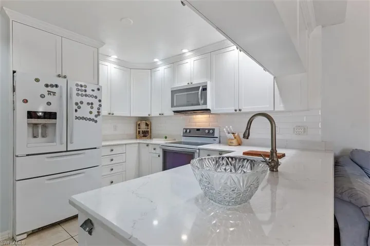 Kitchen featuring white appliances, tasteful backsplash, light stone countertops, white cabinets, and recessed lighting