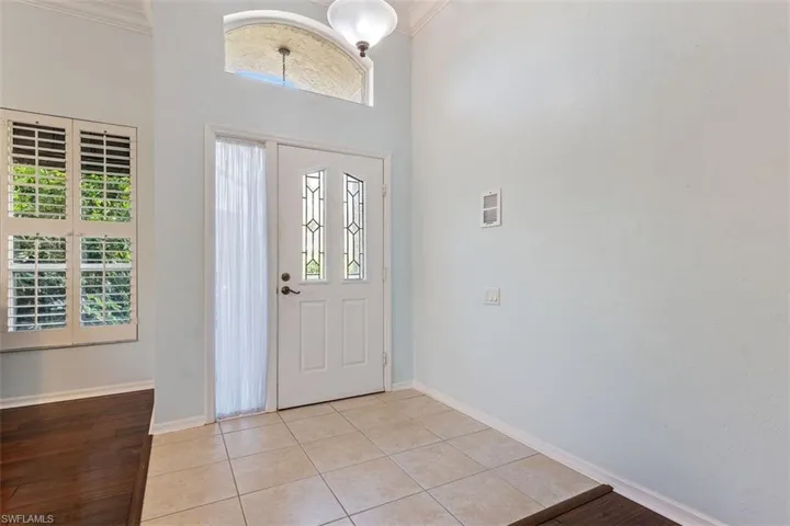 Foyer entrance with ornamental molding, light tile patterned floors, and a towering ceiling