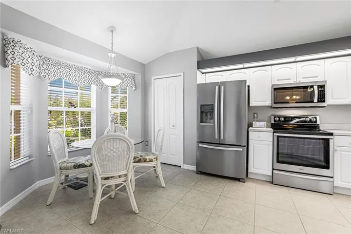Kitchen featuring white cabinets, appliances with stainless steel finishes, pantry, light tile floors, pendant lighting over dining area