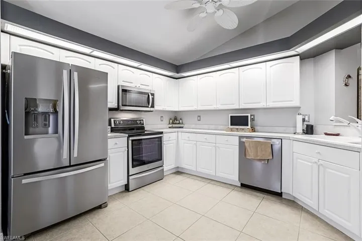 Kitchen with stainless steel appliances, vaulted ceiling, white cabinetry, and ceiling fan