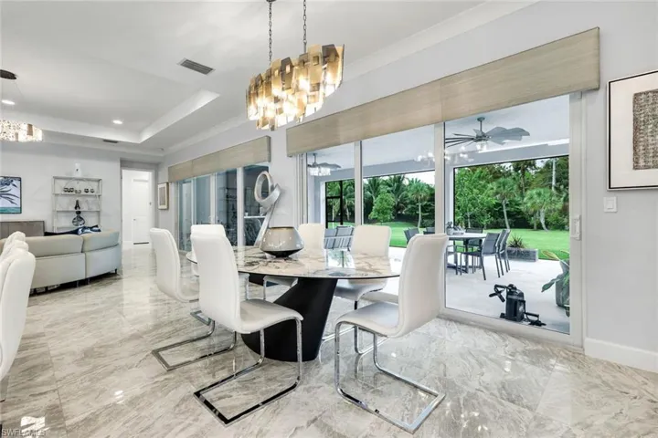 Dining area with a chandelier, light marble finish flooring, and a raised ceiling