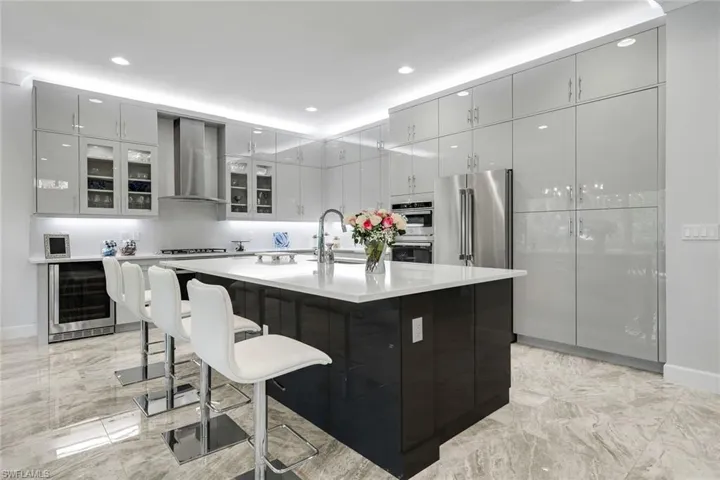 Kitchen featuring a large island, beverage cooler, wall chimney range hood, and recessed lighting