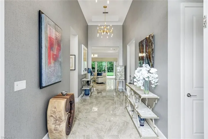 Hallway with a high ceiling, a chandelier, light marble finish flooring, a tray ceiling, and a textured wall paper