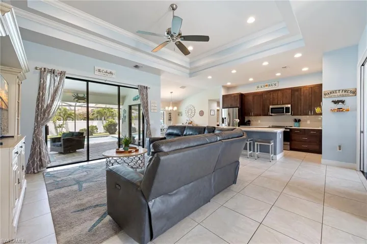 The open concept living area features a coffered ceiling with a ceiling fan, light tile flooring, and sliding glass doors leading to the outdoor space