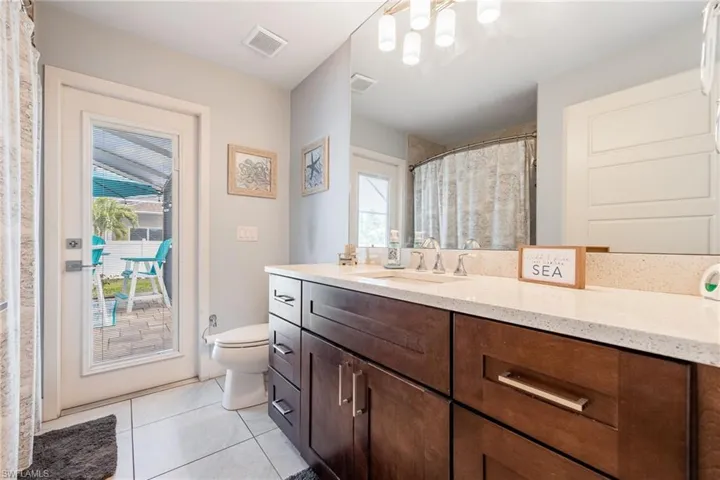Bathroom featuring a dark wood vanity with a light-colored countertop, a white toilet, and a glass-paneled door leading to an outdoor paved patio