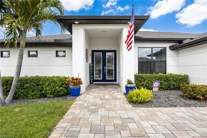 The property features a paver stone walkway leading to the entrance, a dark blue double entry door with glass panels, and a well-maintained lawn with mature landscaping