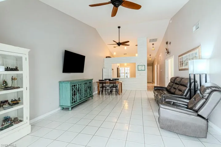 Tiled living room with high vaulted ceiling, built in features, and ceiling fan