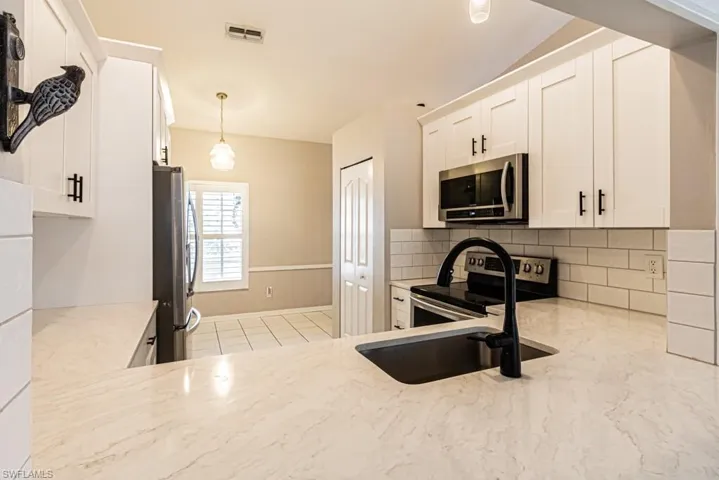 Kitchen featuring stainless steel fridge, white cabinets, plenty of natural light, and vaulted ceiling