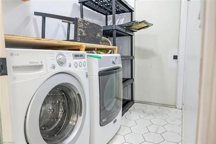 Washroom with washing machine and clothes dryer and light tile patterned floors