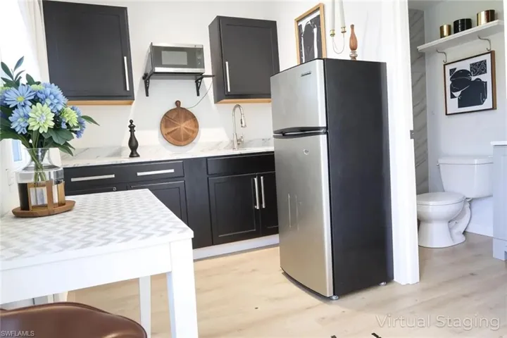Kitchen with stainless steel appliances, dark cabinetry, light wood finished floors, and light stone countertops
