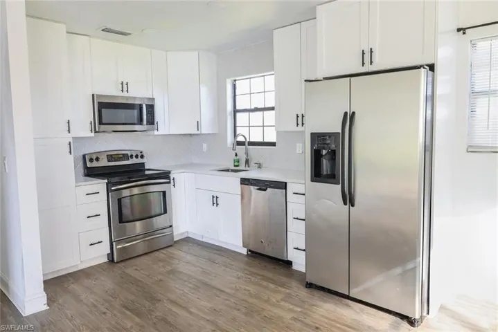 Kitchen featuring appliances with stainless steel finishes, white cabinets, dark wood-style floors, and tasteful backsplash