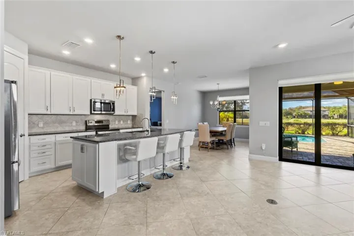 Kitchen with a breakfast bar area, a kitchen island with sink, decorative light fixtures, dark stone counters, and appliances with stainless steel finishes