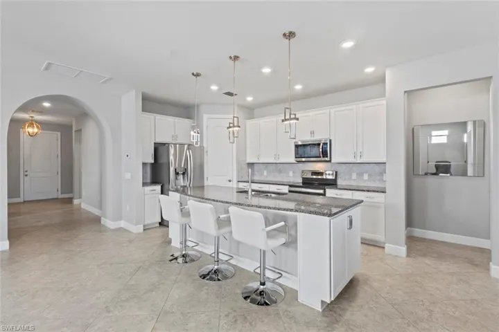 Kitchen featuring white cabinetry, a kitchen bar, dark stone counters, appliances with stainless steel finishes, and a kitchen island with sink