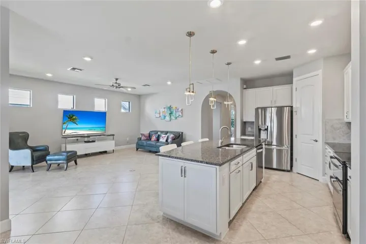 Kitchen with open floor plan, pendant lighting, appliances with stainless steel finishes, white cabinetry, and dark stone countertops